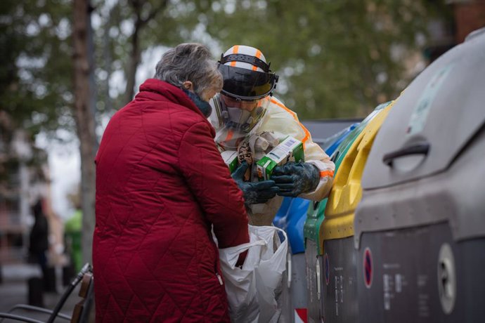 Un treballador que desinfecta i neteja els contenidors d'escombraries de Barcelona ajuda una dona durant la tercera setmana de confinament per la crisi del coronavirus. (arxiu)