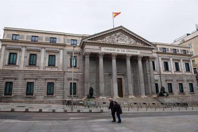 Dos personas mayores pasan junto al Congreso de los Diputados durante el primer día del luto oficial por los fallecidos del COVID-19 decretado por la presidenta madrileña, Isabel Díaz Ayuso, en Madrid (España) a 30 de marzo de 2020.
