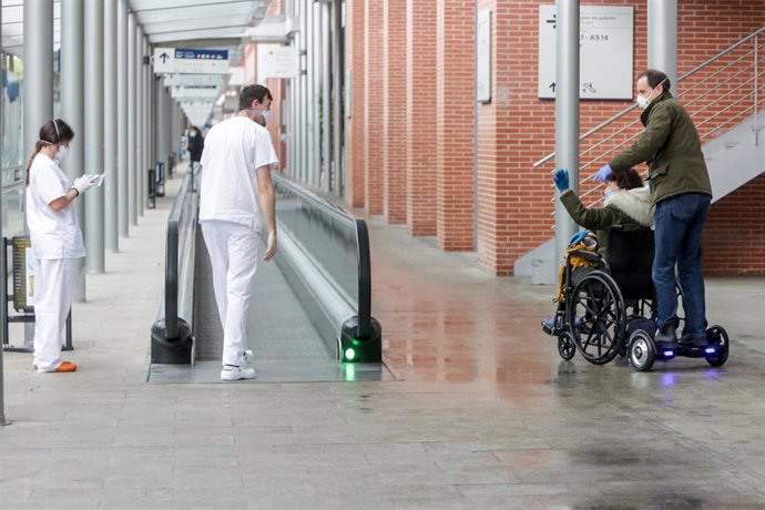 Dos sanitarios protegidos con mascarillas y guantes saludan a una paciente en silla de ruedas recuperada del Covid-19 en un pasillo del Hospital temporal de la Comunidad de Madrid habilitado en IFEMA 