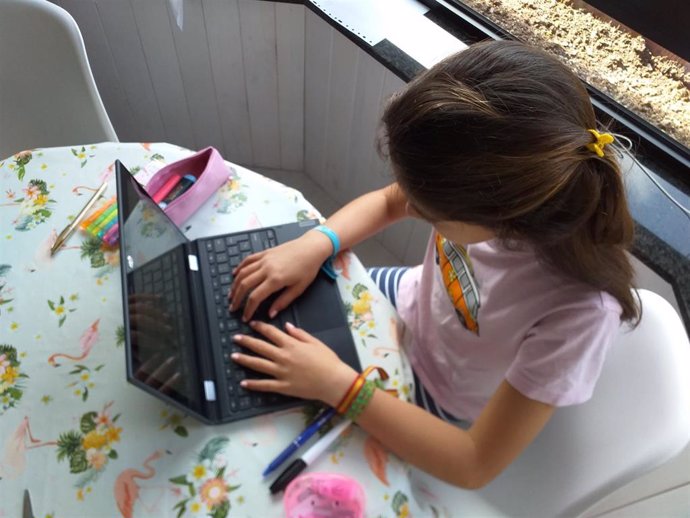 Una niña, haciendo deberes en casa con el ordenador portátil.