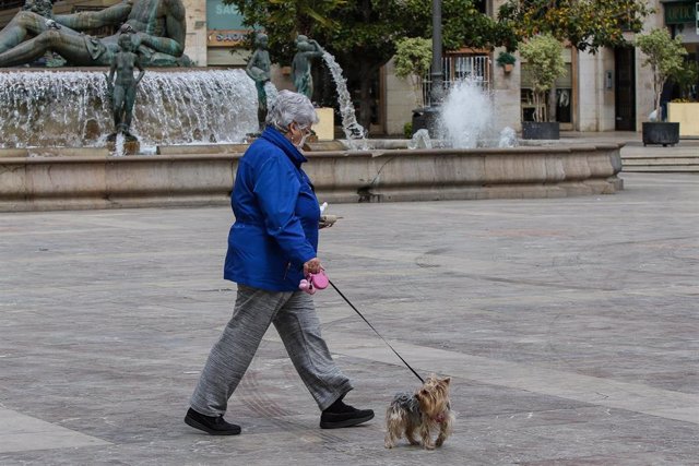 Una mujer con mascarilla pasea a su perro durante el cuarto día del estado de alarma