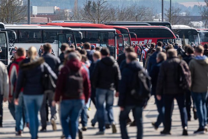 18 March 2020, Bavaria, Dingolfing: BMW employees walk in front of buses during the shift change at the plant. BMW stops car production in its European plants and in South Africa for four weeks due to the coronavirus crisis. Photo: Armin Weigel/dpa