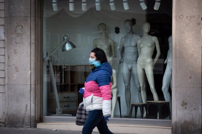 Una dona protegida amb una mascarilla passa al costat d'un aparador d'una botiga tancada durant el nov dia laborable des que es va decretar l'estat d'alarma a conseqüncia del coronavirus, a Barcelona/Catalunya (Espanya) a 26 de mar de 2020.