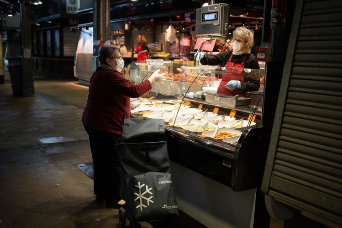 Una dona amb mascarilla compra en un lloc d'un mercat i és atesa per una altra dona protegida també amb una mascarilla, durant el tercer dia laborable de l'estat d'alarma per coronavirus, a Barcelona/Catalunya (Espanya) a 18 de mar de 2020.