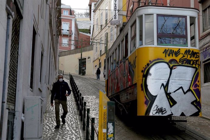 Hombre con mascarilla por el coronavirus junto a un tranvía en Lisboa
