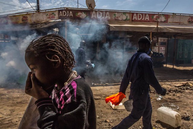 Varias personas caminan por un mercado de Dakar, Senegal, mientras un trabajador desinfecta sus calles.