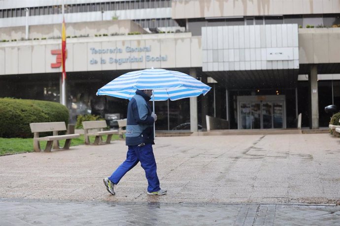 Un hombre con paraguas pasa frente a una oficina de la Tesorería General de la Seguridad Social