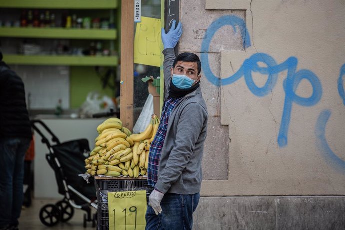 Un home protegit amb mascarilla i guants en la porta del seu establiment d'alimentació, durant el primer dia laborable de la segona setmana des que es va decretar l'estat d'alarma, a Barcelona/Catalunya (Espanya) a 23 de mar de 2020.