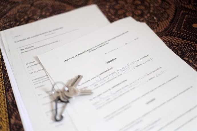 Unas llaves sobre un contrato de compraventa de vivienda y un contrato de arrendamiento (alquiler) de una habitación en una vivienda compartida.