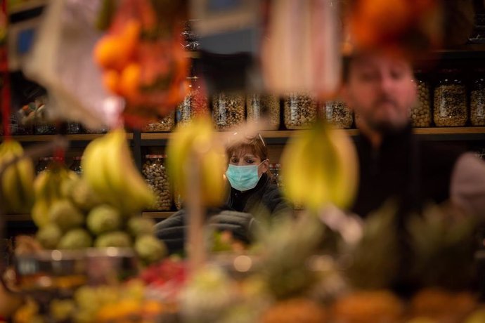 Una mujer protegida con mascarilla espera a ser atendida en una frutería durante el segundo día laborable del estado de alarma por el coronavirus, en Barcelona (España), a 17 de marzo de 2020.