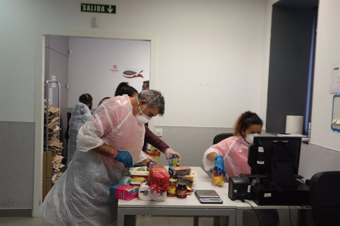 Voluntarios protegidos con guantes, mascarilla y traje de plástico registran los alimentos de las donaciones que posteriormente pasarán a ser vendidos en el  economato solidario de Cáritas situado en la calle Bravo Murillo de Madrid