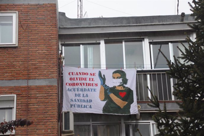 Sábana blanca con un dibujo de una sanitaria protegida con mascarilla y guantes y unas letras que dicen 'Cuando se olvide el coronavirus, acuérdate de la Sanidad Pública', en una ventana de Madrid por el Día Mundial de la Salud