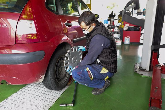 Un trabajador de un taller protegido con una mascarilla arregla la rueda de un coche. 