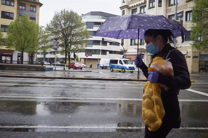 Una mujer se protege de la lluvia con un paraguas mientras camina con una bolsa de patatas durante el Martes Santo y la cuarta semana del estado de alarma decretado por el Gobierno por la crisis del coronavirus, en Pamplona/Navarra (España) a 7 de abril