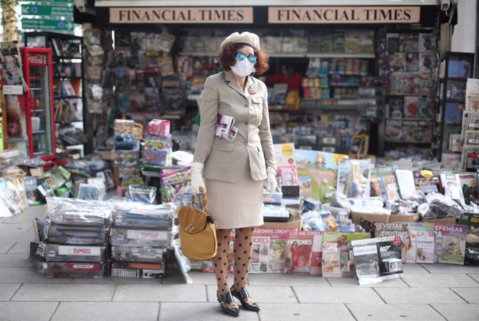 Una mujer protegida con mascarilla y con una revista en su brazo posa al lado de uno de los quioscos de Madrid