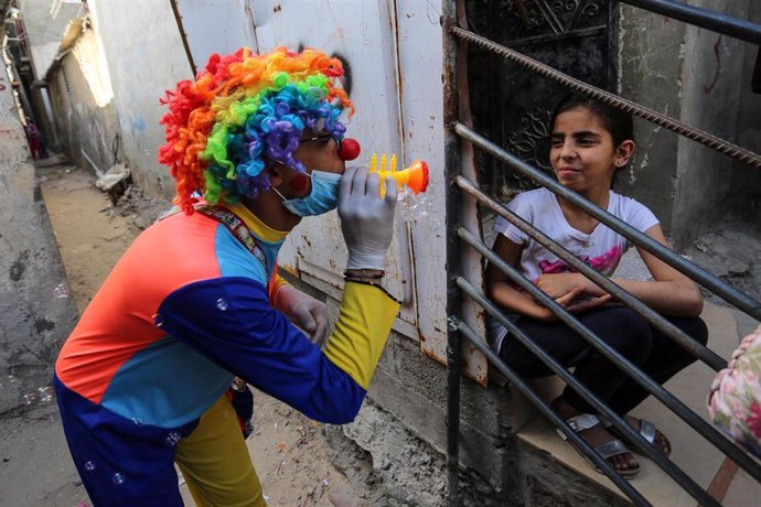 Un payaso con mascarilla entretiene a una niña palestina en confinamiento