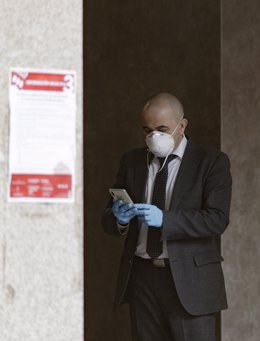 Un home amb mascarilla i guants manipula un mbil durant l'emergncia sanitria del Covid-19. 