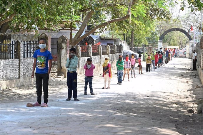 Niños con mascarilla por el coronavirus hacen cola en India para conseguir el menú escolar 