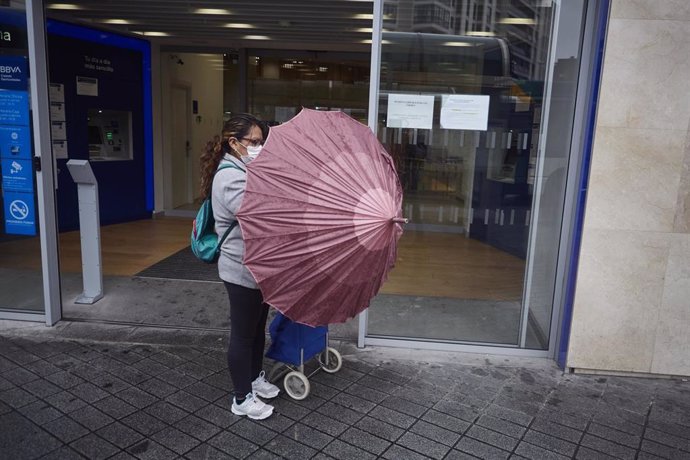 Una mujer con mascarilla se protege de la lluvia con un paraguas.