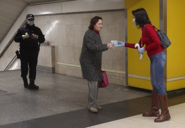 Un agente de la Policía Nacional vigila el reparto de mascarillas de una voluntaria de la Cruz Roja a pasajeros en el metro de Avenida de América.