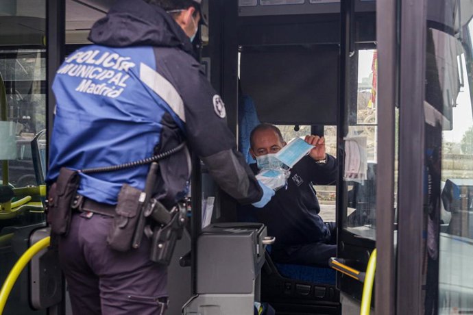 Un agente de la Policía Municipal de Madrid reparte mascarillas al conductor de un autobús de la línea 9 de la EMT 