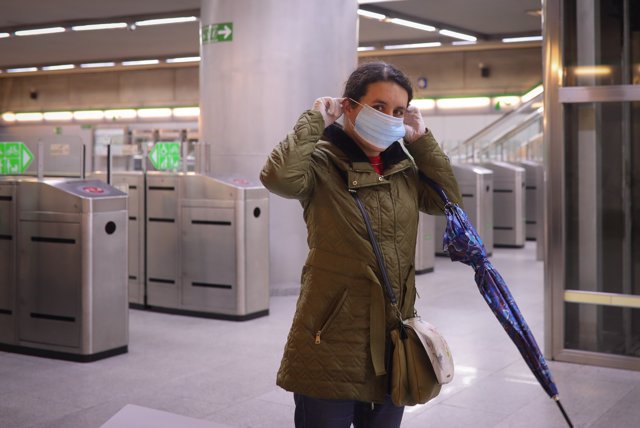 Una mujer se pone una mascarilla tras recibirla de Protección Civil a la entrada del metro de Sevilla