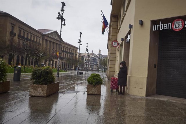 Una mujer camina bajo la lluvia con el carro de la compra frente al Palacio del Gobierno de Navarra durante el Martes Santo y la cuarta semana del estado de alarma decretado por el Gobierno por la crisis del coronavirus, en Pamplona/Navarra (España) a 7 d