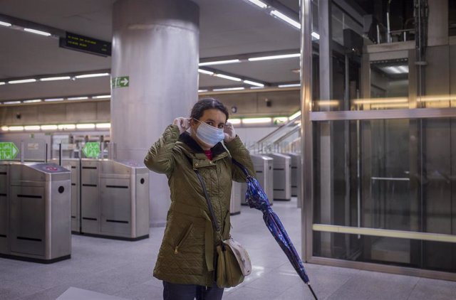 Una mujer se pone una mascarilla tras recibirla de Protección Civil a la entrada del metro de Sevilla.