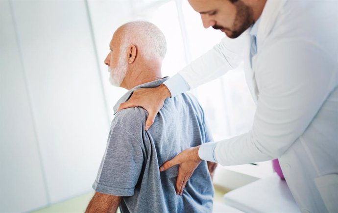 Médico examina la espalda a un paciente mayor con dolor.