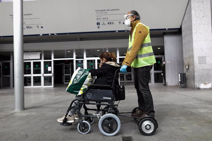 Un trabajador sanitario protegido lleva en silla de ruedas al exterior del hospital de campaña montado en Ifema