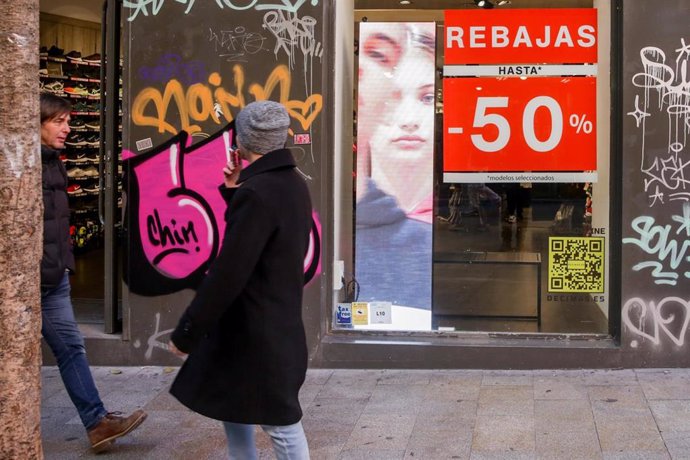 Dos hombres pasean junto a una tienda en Madrid, en la que se ofertan rebajas de hasta un 50%.