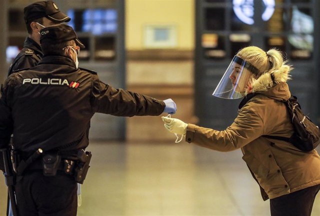Un policía nacional entrega una mascarilla a una mujer en el vestíbulo de la estación del Norte de Valencia el día en el que se reactiva la actividad laboral no esencial en las empresas cuyos empleados no puedan teletrabajar. 14 de abril de 2020.
