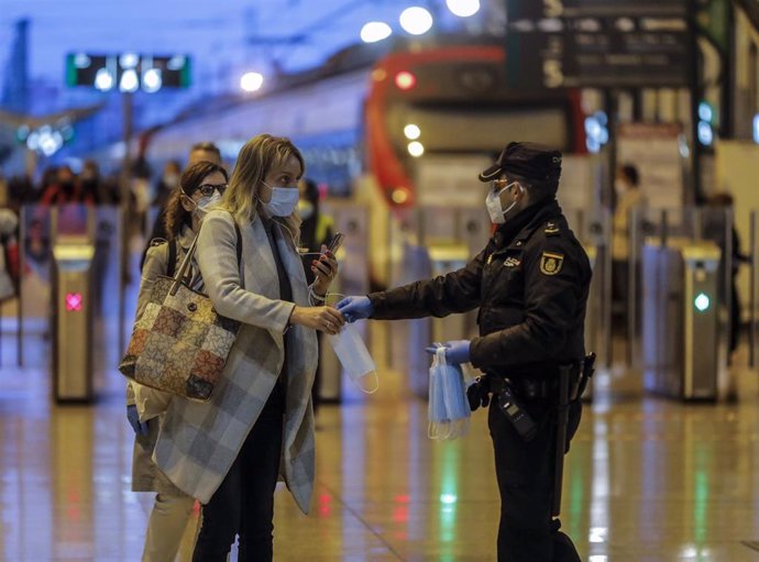Un policía nacional entrega una mascarilla a una mujer en el vestíbulo de la estación del Norte de Valencia el día en el que se reactiva la actividad laboral no esencial en las empresas cuyos empleados no puedan teletrabajar