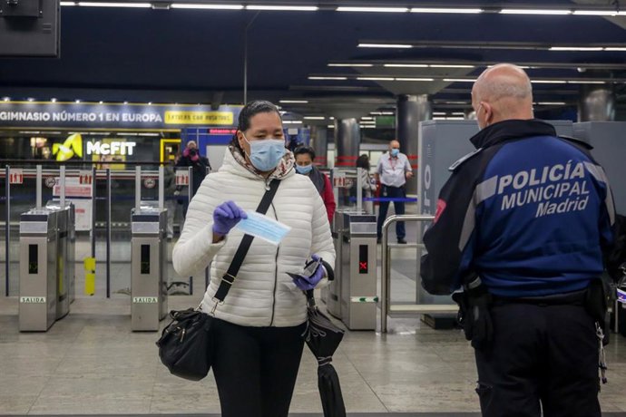 Un agente reparte mascarillas a los pasajeros que cogen el metro en la estación de metro de Nuevos Ministerios