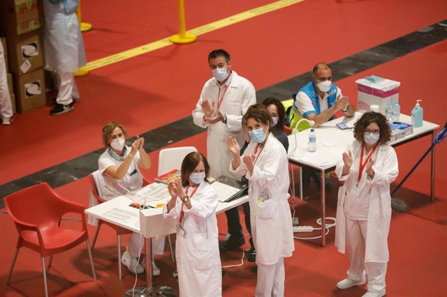 Trabajadores sanitarios protegidos con mascarilla aplauden en el interior del hospital de campaña montado en IFEMA.