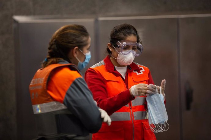 Una voluntaria de Cruz Roja habla con una vigilante de seguridad de la estación catalana de Diagonal, donde están entregando mascarillas a los viajeros el día en el que se reactiva la actividad laboral no esencial en Cataluña en las empresas cuyos emple