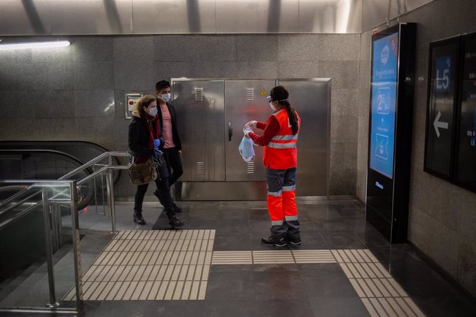 Una voluntaria de Cruz Roja entrega mascarillas a los viajeros que caminan por la estación catalana de Diagonal el día en el que se reactiva la actividad laboral no esencial en Cataluña en las empresas cuyos empleados no puedan teletrabajar, cuando se c