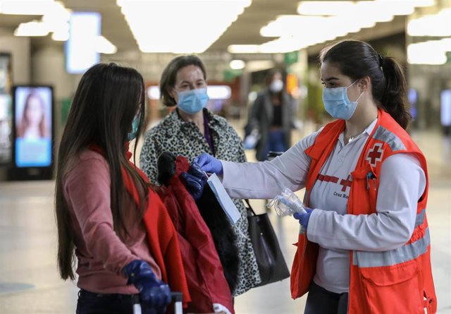 Voluntarios de Cruz Roja entregan mascarillas a pasajeros en la estación de Cercanías de Atocha, en Madrid