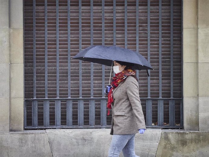 Una mujer con mascarilla camina protegiéndose con un paraguas por la lluvia en una imagen de archivo 