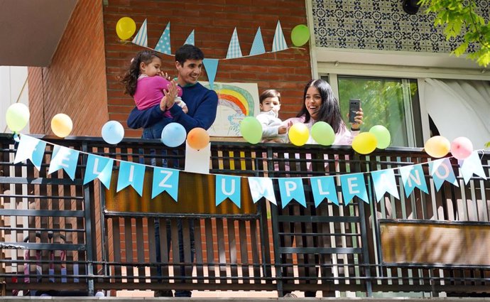 Una familia con hijos saluda desde la terraza la llegada de la Policía Municipal de Sevilla para que le felicite por su cumpleaños durante el confinamiento por la pandemia de coronavirus