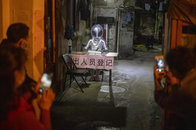 Una persona ataviada con un disfraz de ovni posa desde uno de los escritorios de registro de los ciudadanos de un barrio de Shanghai ante las cámaras de los teléfonos móviles de sus atónitos residentes.