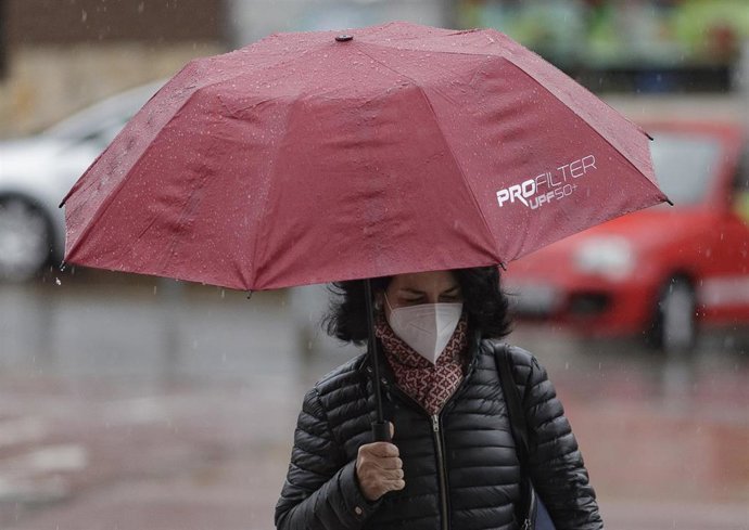 Transeúntes protegidos con mascarilla y un paraguas caminan por las calles 