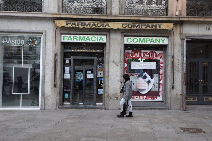 Una mujer protegida con mascarilla y guantes pasa delante de una Farmacia. En Madrid (España) a 14 de abril de 2020.