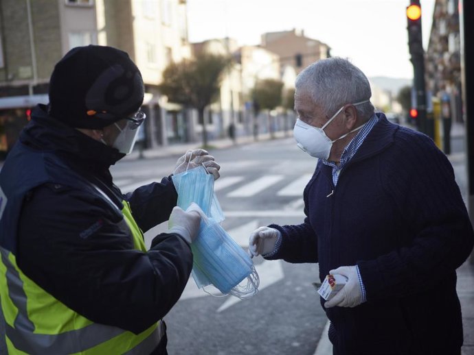Un agente de la Policía Nacional reparte una mascarilla a un hombre durante el día 32 del estado de alarma y dos días después de que se haya reactivado la actividad laboral no esencial en las empresas cuyos empleados no puedan teletrabajar, en Pamplona/