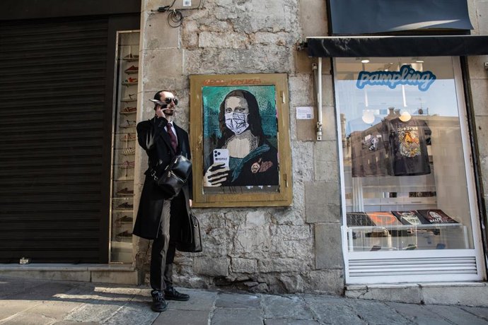 Un hombre habla por teléfono junto a una pintura de una Gioconda con un móvil y una mascarilla, obra del grafitero TV Boy llamada 'Mobile World Virus', en Barcelona/Catalunya (España) a 20 de febrero de 2020.