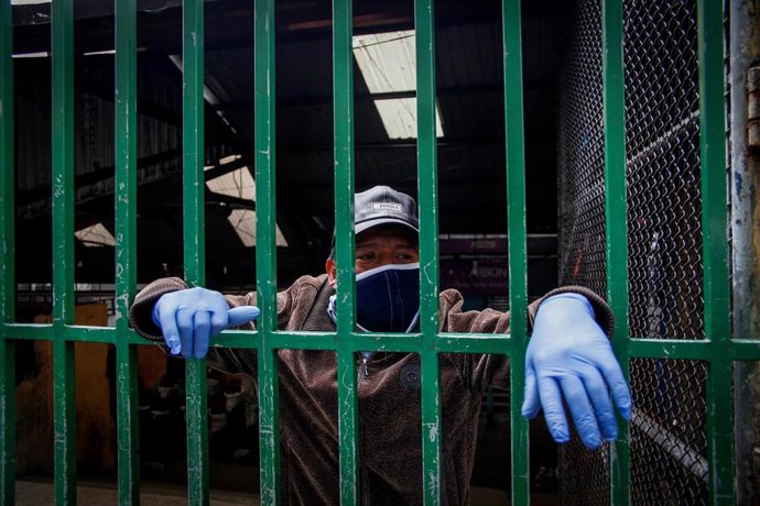 Un ciudadano ecuatoriano observa tras una verja las medidas de seguridad que ejecutan las autoridades en el distrito de San Roque, en Quito, para intentar frenar el avance del Covid-19.