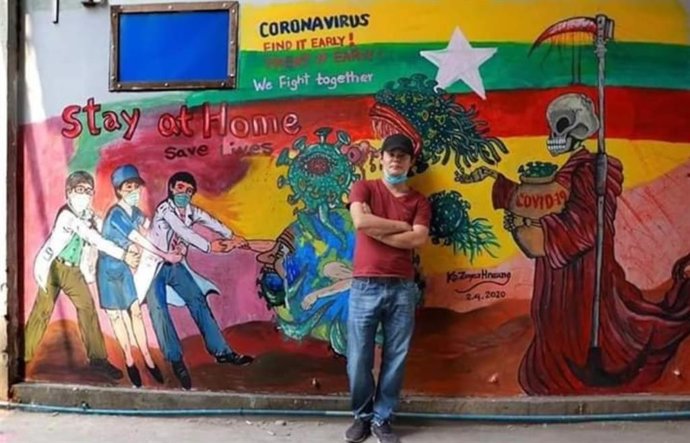El artista callejero birmano Zayar Hnaung posa junto al moral denunciado por ofender a los sentimientos religiosos.