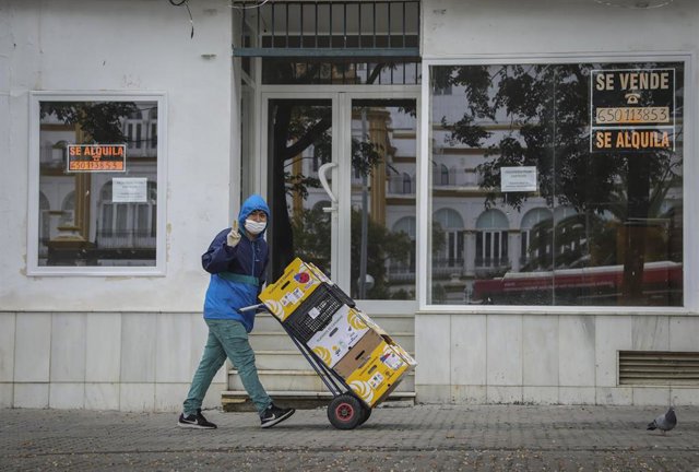Un trabajador realiza el reparto protegido con una capucha bajo la lluvia  en la quinta semana del estado de alarma por el coronavirus, Covid-19. En Sevilla (Andalucía, España), a 15 de abril 2020.