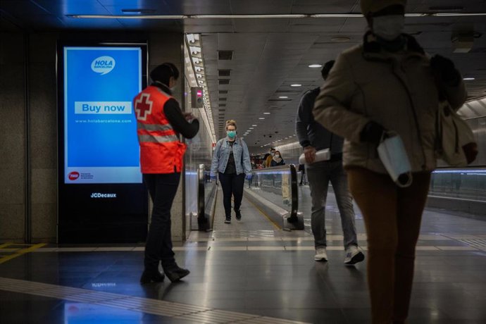Una voluntaria de Cruz Roja entrega mascarillas a los viajeros que caminan por la estación catalana de Diagonal el día en el que se reactiva la actividad laboral no esencial en Cataluña, en Barcelona (Catalunya, España), a 14 de abril de 2020.