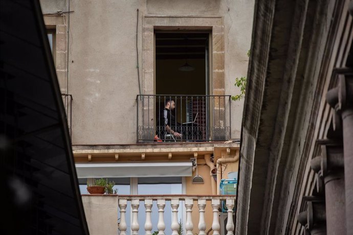 Un joven utiliza su ordenador portátil en su terraza durante el segundo día laborable del estado de alarma por el coronavirus, en Barcelona (España)